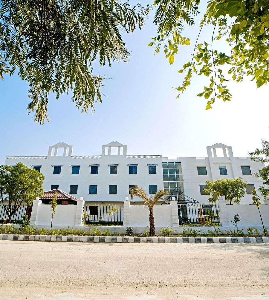 Front view of Grassfield Riveria Resort, Jaipur, surrounded by trees and clear skies, showcasing the modern building facade.