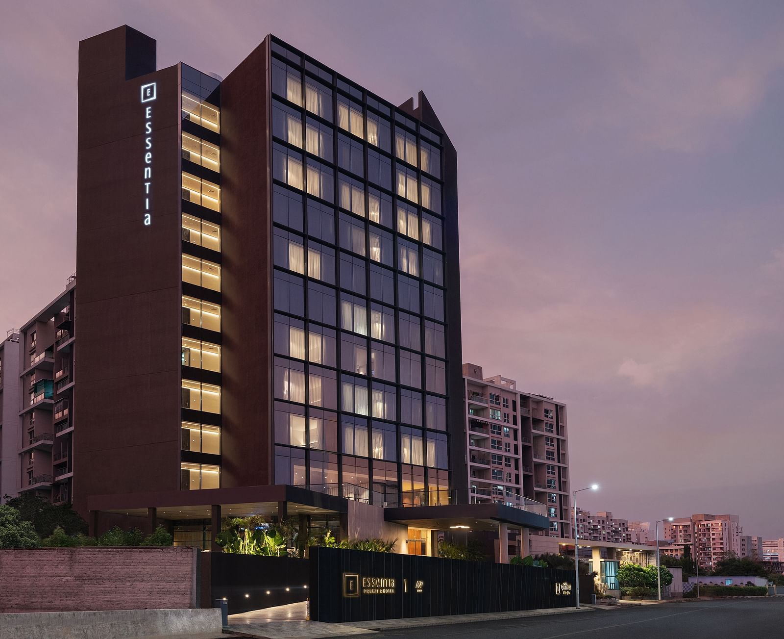Facade of Essentia Premiere, Pune with lights on during twilight.