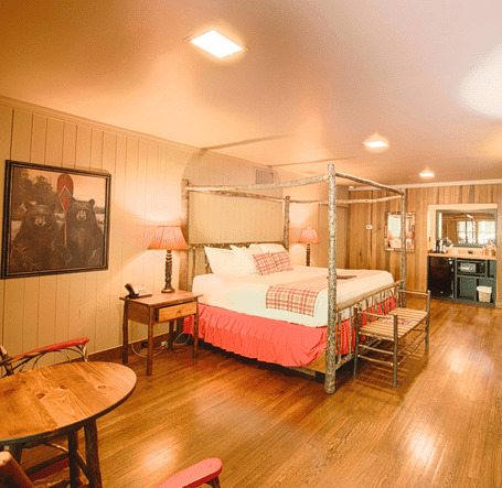 a bedroom with cozy interiors and wooden flooring featuring a double bed along with seating area with a round coffee table - Historic Tapoco Lodge