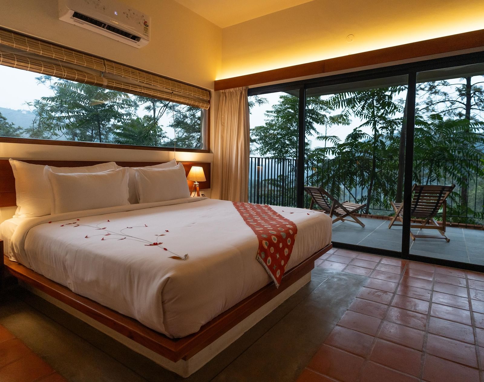  A well-appointed bedroom at Vaasta Vagamon featuring a large bed with a decorative runner, and expansive windows overlooking a scenic view.