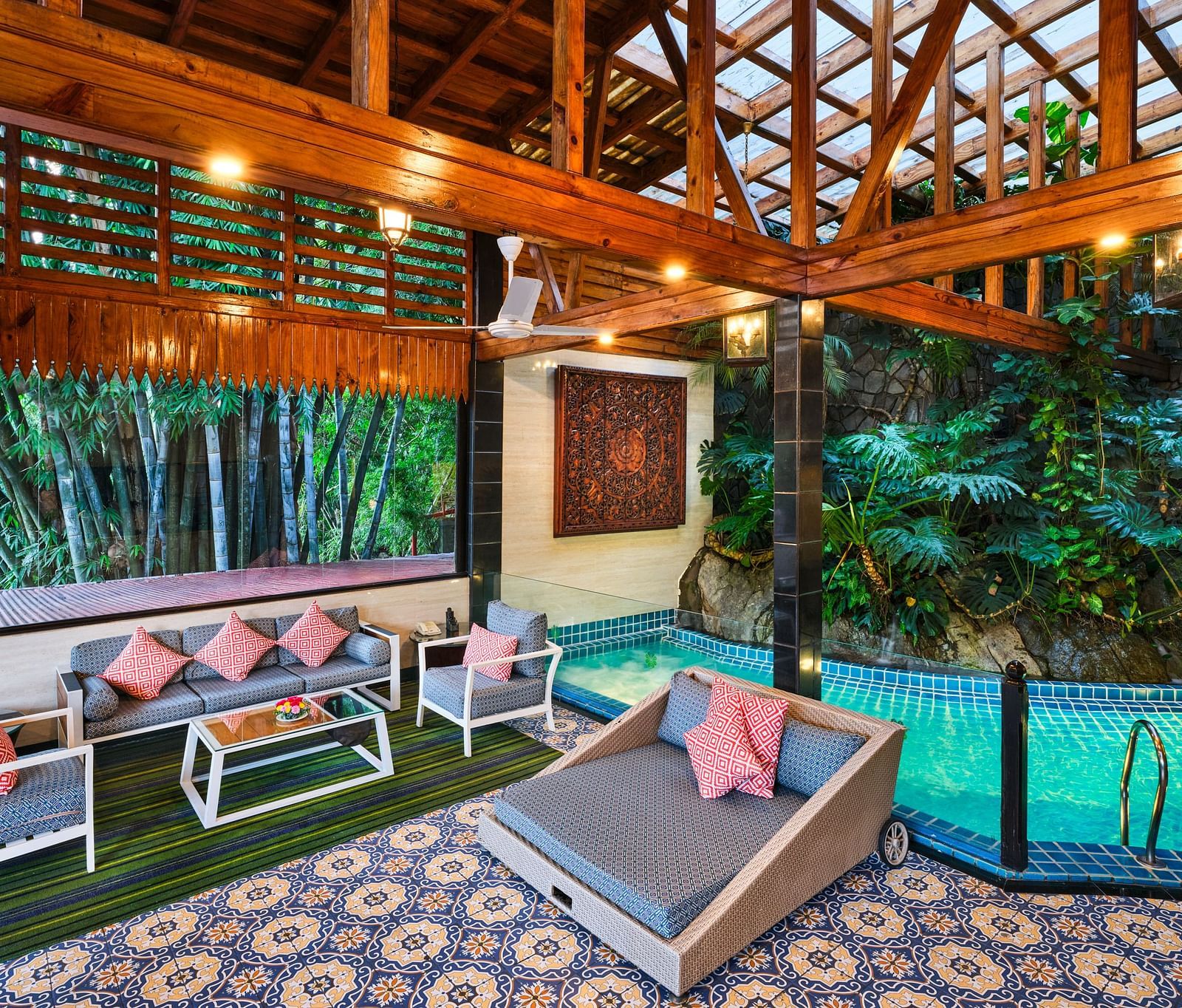 An artistic luxurious outdoor space of Grand Villa featuring a pool, patterned tile floor, outdoor seating, wooden structures, an lush greenery.