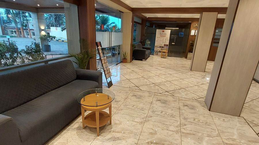 A hotel lobby area with a grey sofa, a small round wooden table, and a tiled floor leading towards the entrance - Lords Eco Inn Dahej