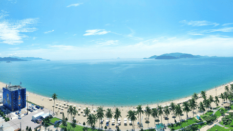 An aerial view of the Nha Trang's coastline with the beach, trees, road and islands in the far distance seen