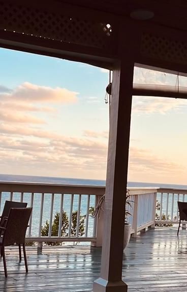 The outdoor patio at A Stone's Throw Away overlooking at the ocean with a beautiful evening sky in the background along with several dining tables set on the patio.