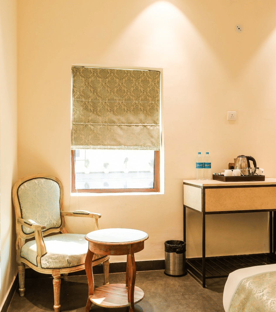 Bedroom with chair, table, bed, and window with blinds at Beelwa Palace, Jaipur