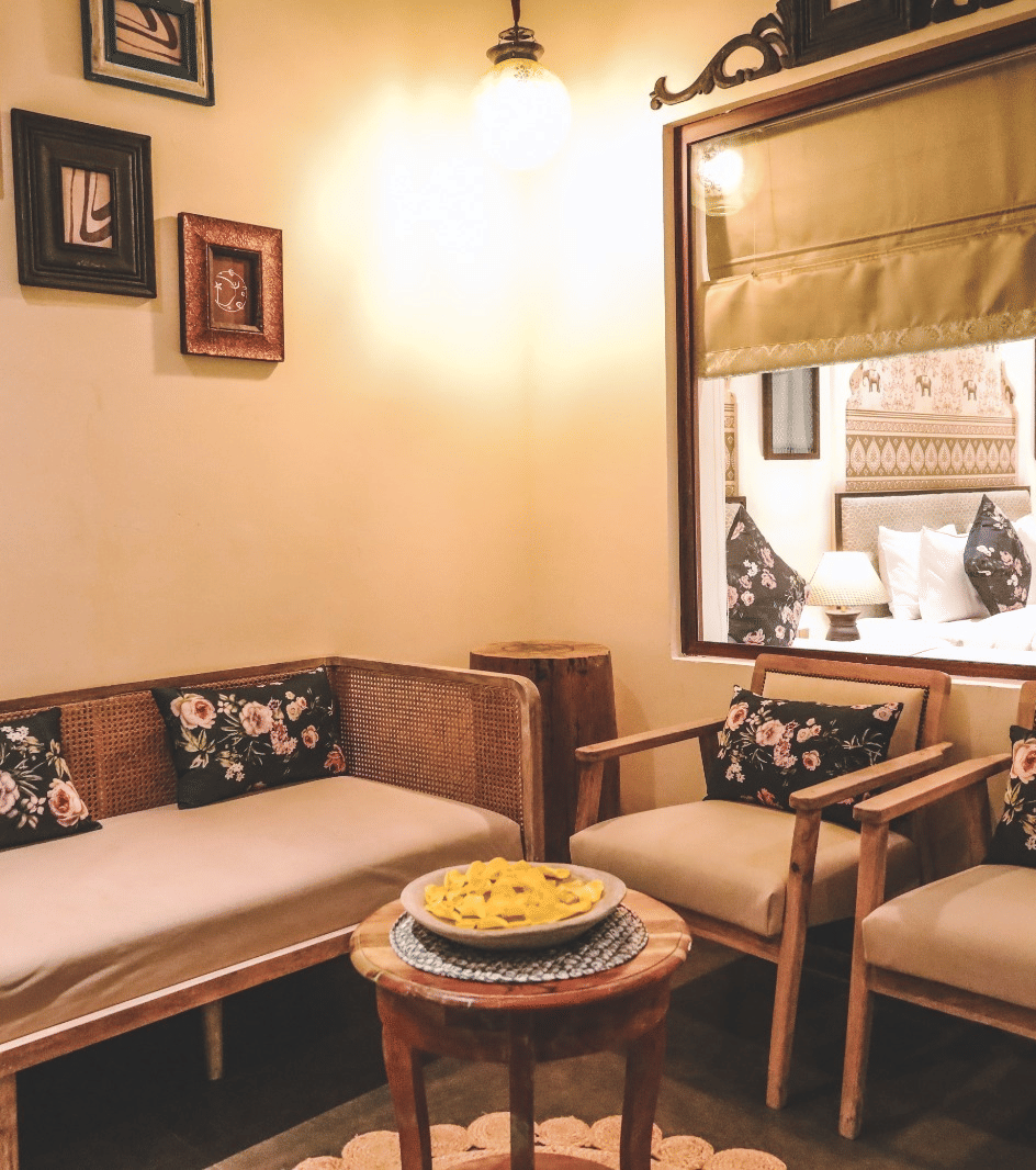 Small seating area with a sofa, chairs, wall frames, and a window at Beelwa Palace, Jaipur