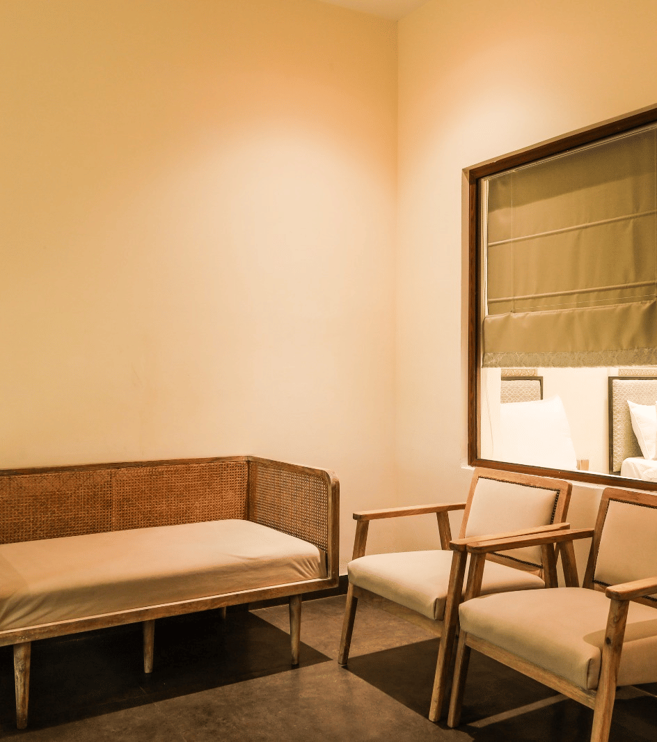 Simple room with wooden sofa, chairs, and window blinds at Beelwa Palace, Jaipur