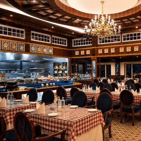 Tiffany restaurant with red-and-white chequered tablecloths, blue high-back chairs, an open live kitchen and a chandelier at MAYFAIR Himalayan Spa Resort, Kalimpong.