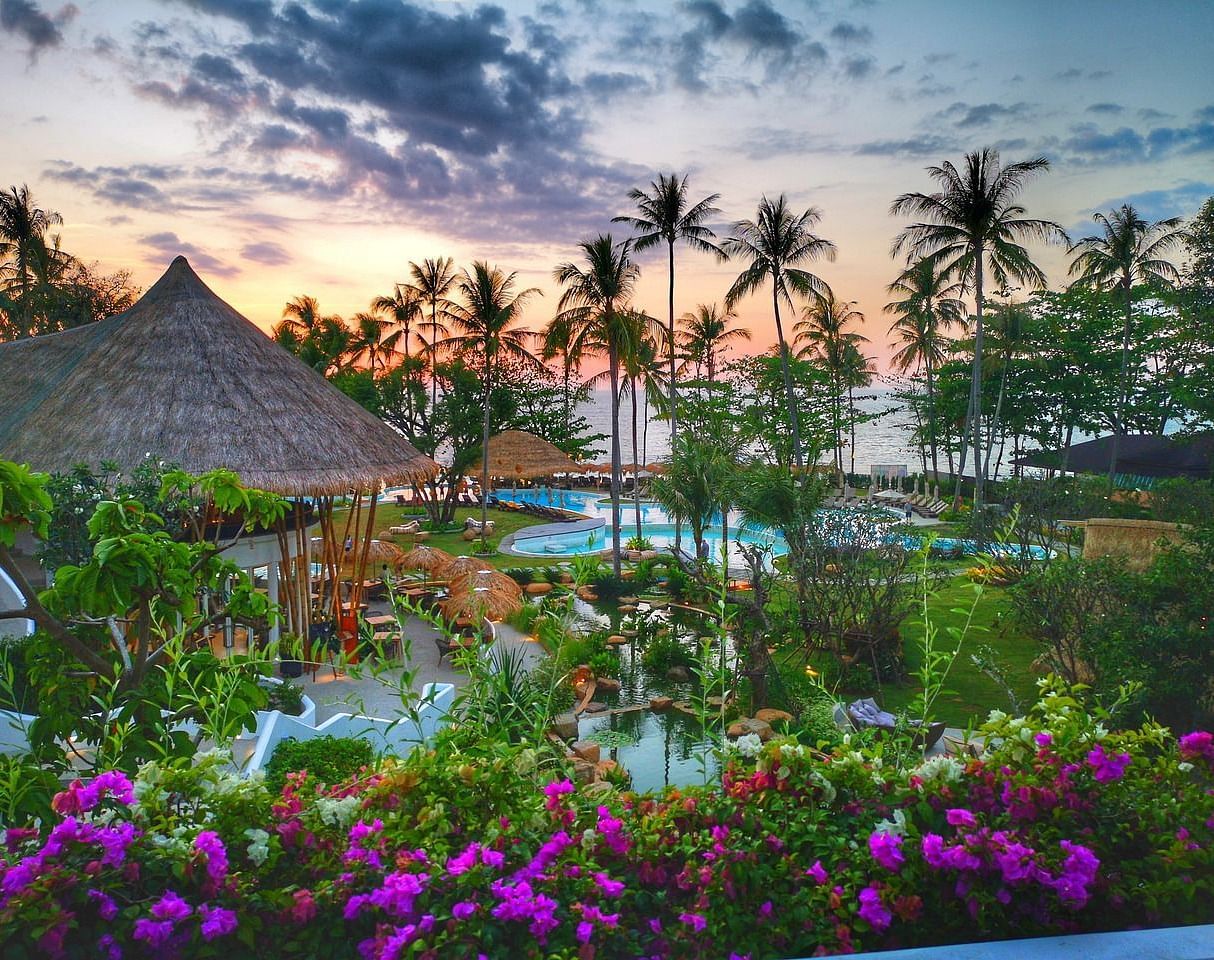 Tropical resort at sunset with lush vegetation and thatched-roof structures.