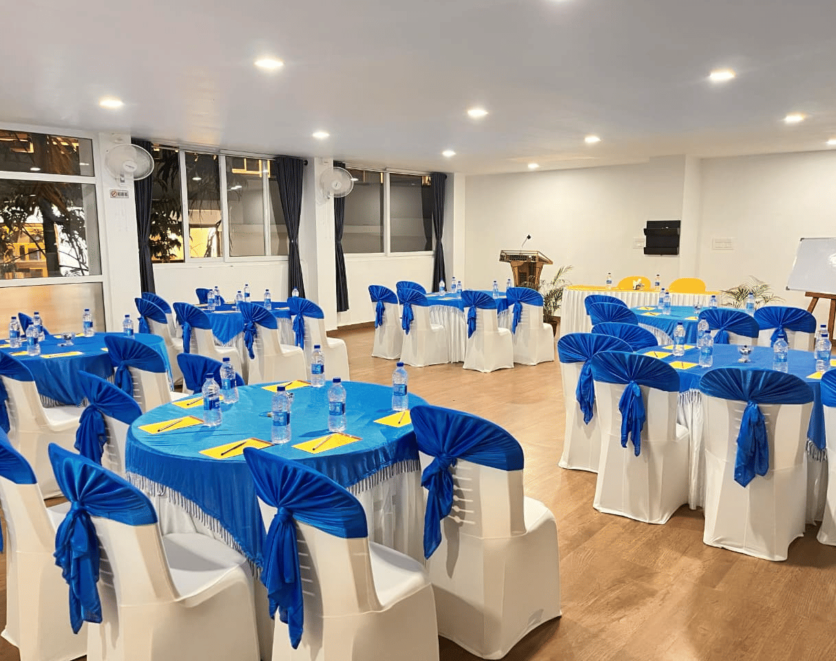 A large indoor event hall set up with many round tables and chairs, all decorated with bright blue and yellow cloth coverings at Coorg Orange Blossom Resort and Spa.
