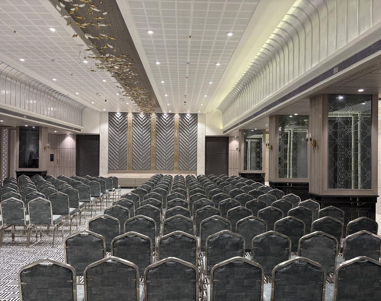 A large room is set up with numerous grey chairs in rows facing a front - Melior Inn