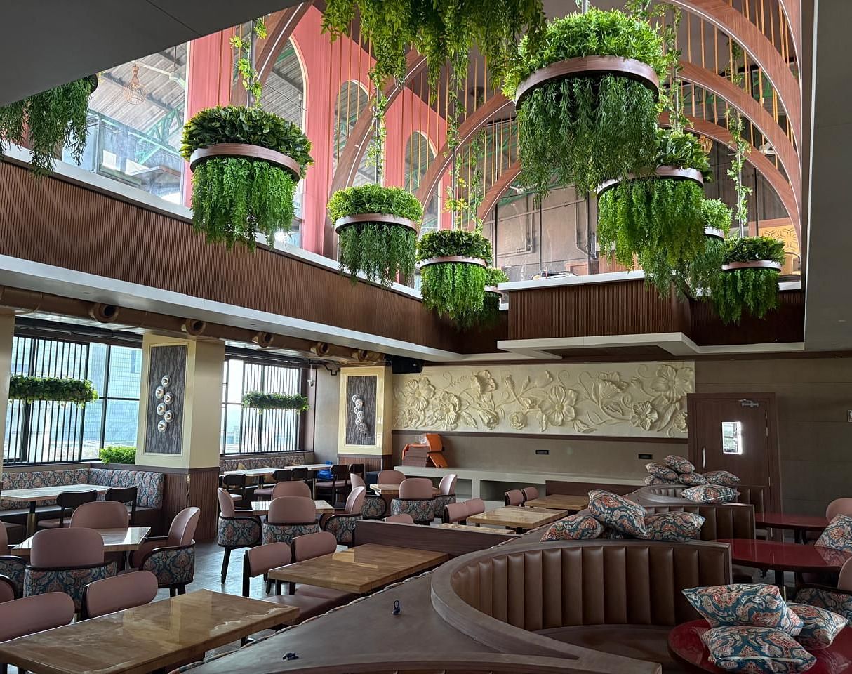 A warmly lit restaurant area with booth seating, wooden tables, and hanging plants as part of the decor - Melior Inn