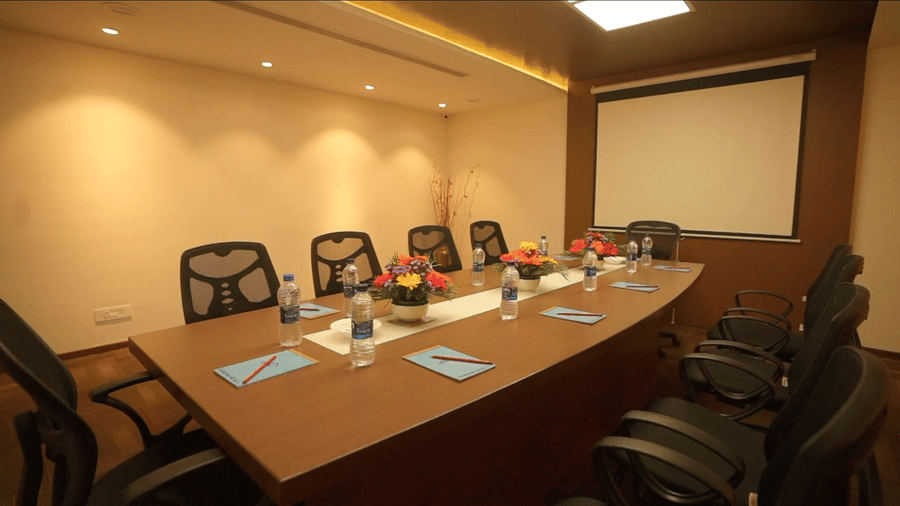 The boardroom Pluto at S Hotels, Chennai, featuring a long conference table with chairs arranged around it and modern lighting.