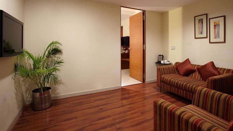 A cosy hotel suite featuring striped sofas, wooden flooring, a flat-screen TV, and lush greenery adding a touch of tranquillity - The President Hotel Jayanagar, Bangalore