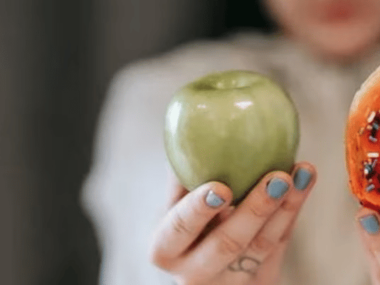 a woman holding an apple in one hand and a doughnut in the other