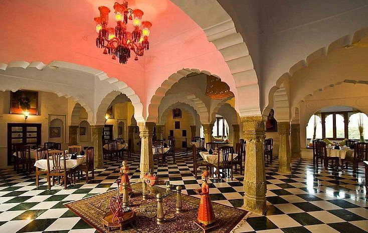 An elegant dining hall at Fort Barli, with arched ceilings, checkered floors, and a vibrant chandelier, blends historical architecture with a refined dining experience.