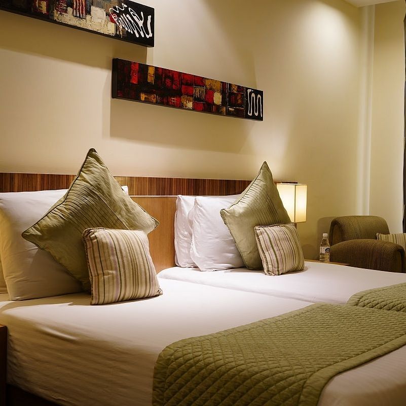 Standard Room featuring twin beds with green duvets and pillows at Shervani Nehru Place, New Delhi