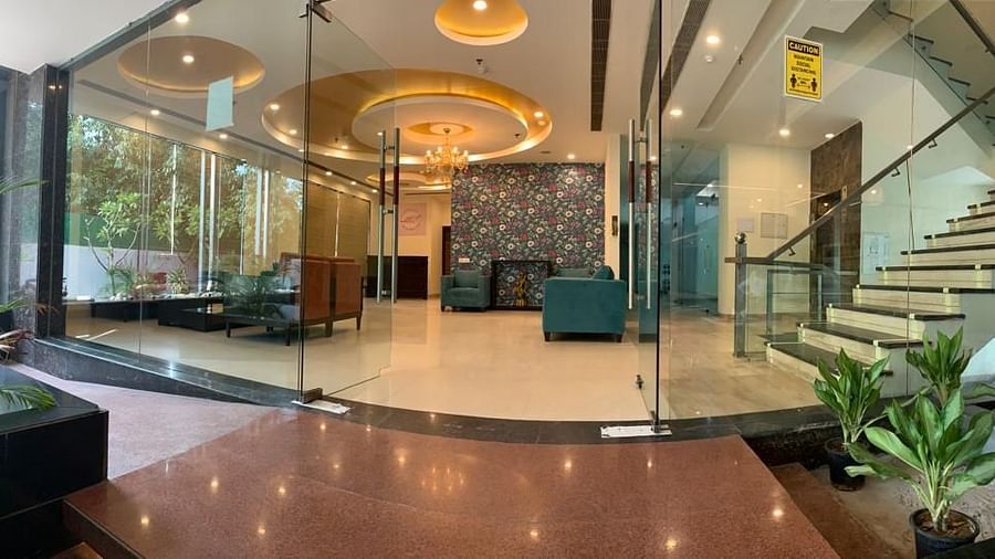 A glass-walled entrance with a spiral staircase, plants, and a unique ceiling design, creating a grand entrance - VITS Gurugram
