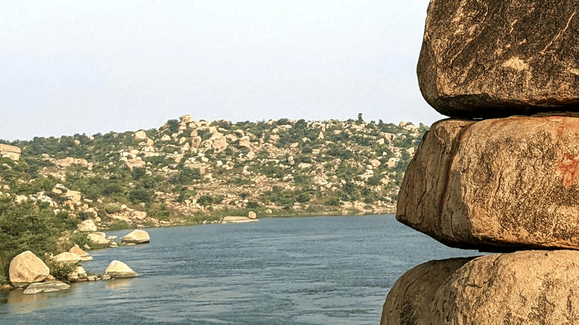 Stacked boulders perched on a cliff edge overlooking a wide river.