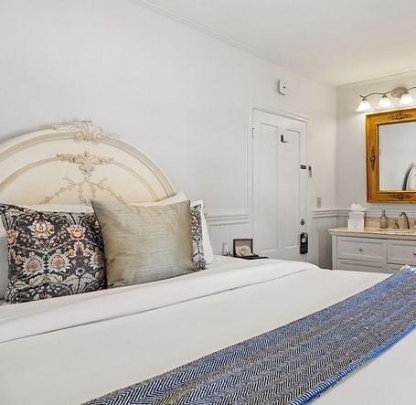 A bedroom with ornate headboard, a mirror, table and blue-accented runner at Hartstone Inn