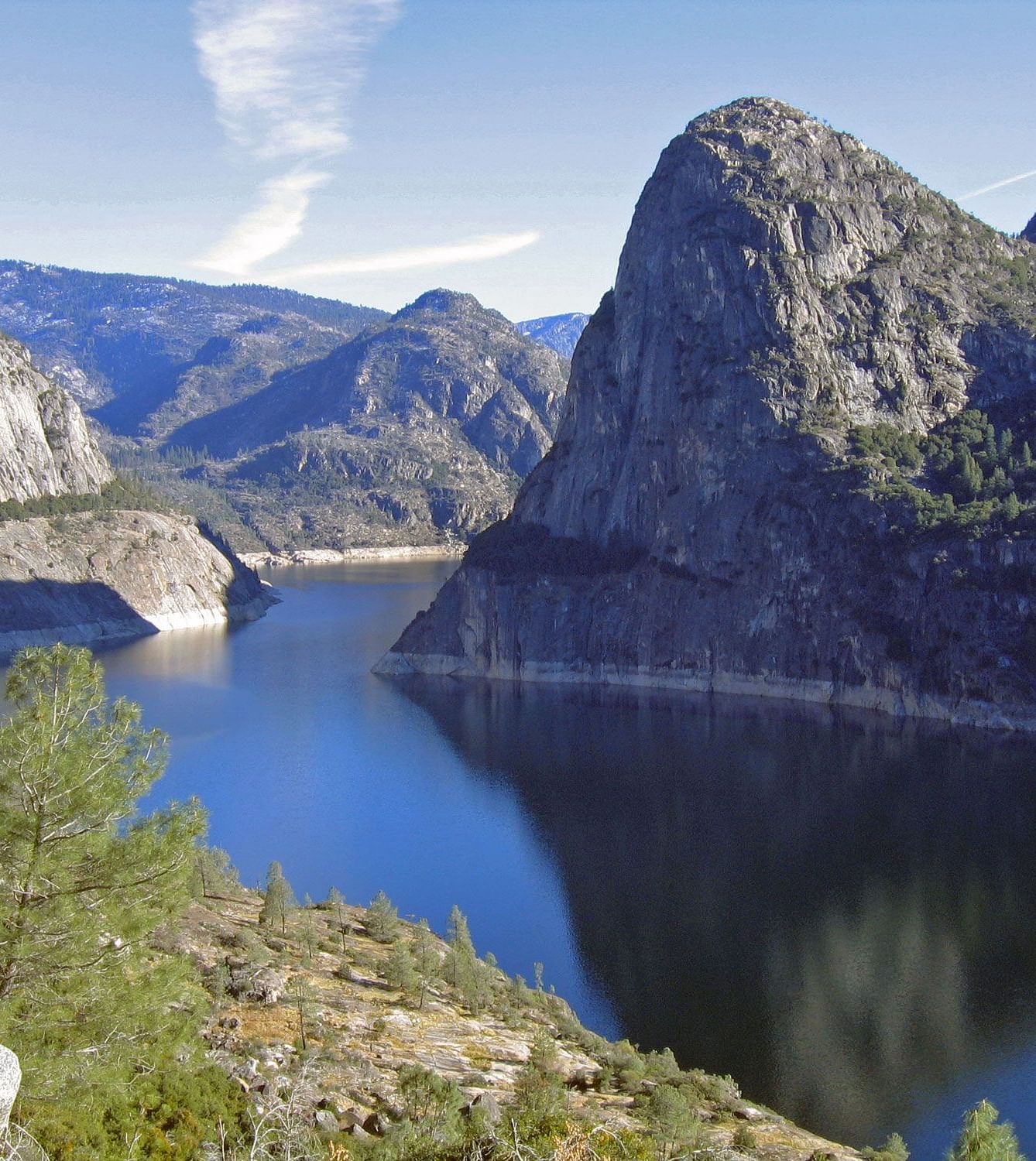 View of the Hetch Hetchy Reservoir, showcasing water flowing between majestic natural mountains under a bright, sunny sky