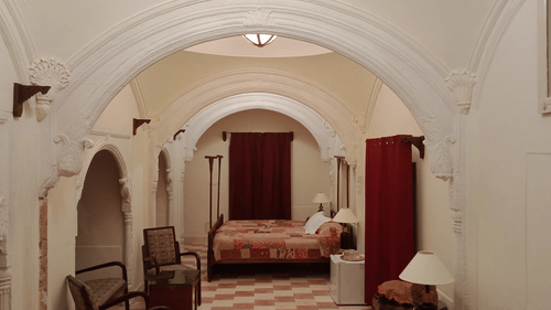 Arched doorways lead through the white interiors of Tijara Fort-Palace - 19th Century, Alwar, revealing a bedroom with a patterned bed and seating.