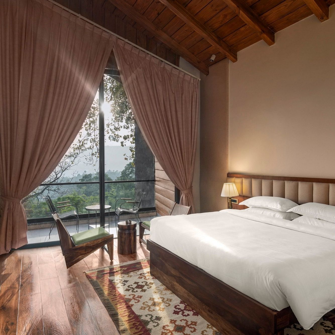 A cosy bedroom with a wooden floor and ceiling, large draped window with a scenic view, and a comfortable sitting area - The Samai, Bhimtal
