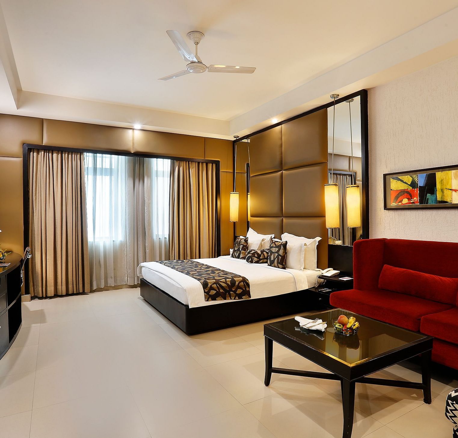 A spacious junior suite with a sleek design, featuring a large bed, red sofa at The Manor, Bareilly