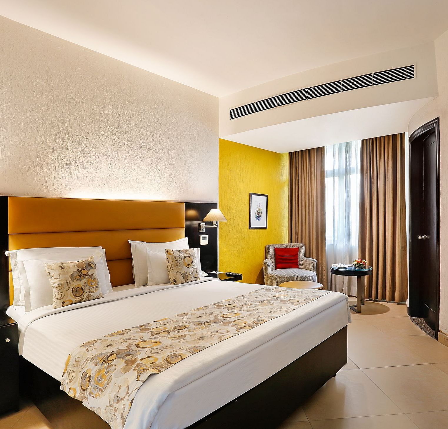 A modern hotel room with a plush white bed, vibrant yellow accent wall and contemporary furnishings - The Manor, Bareilly