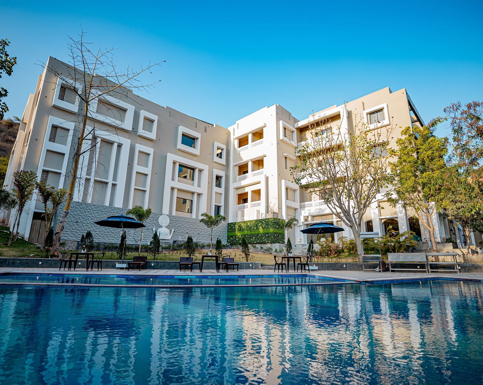 Facade of Essentia Luxury Resort and Spa, Udaipur with the pool in front of it.