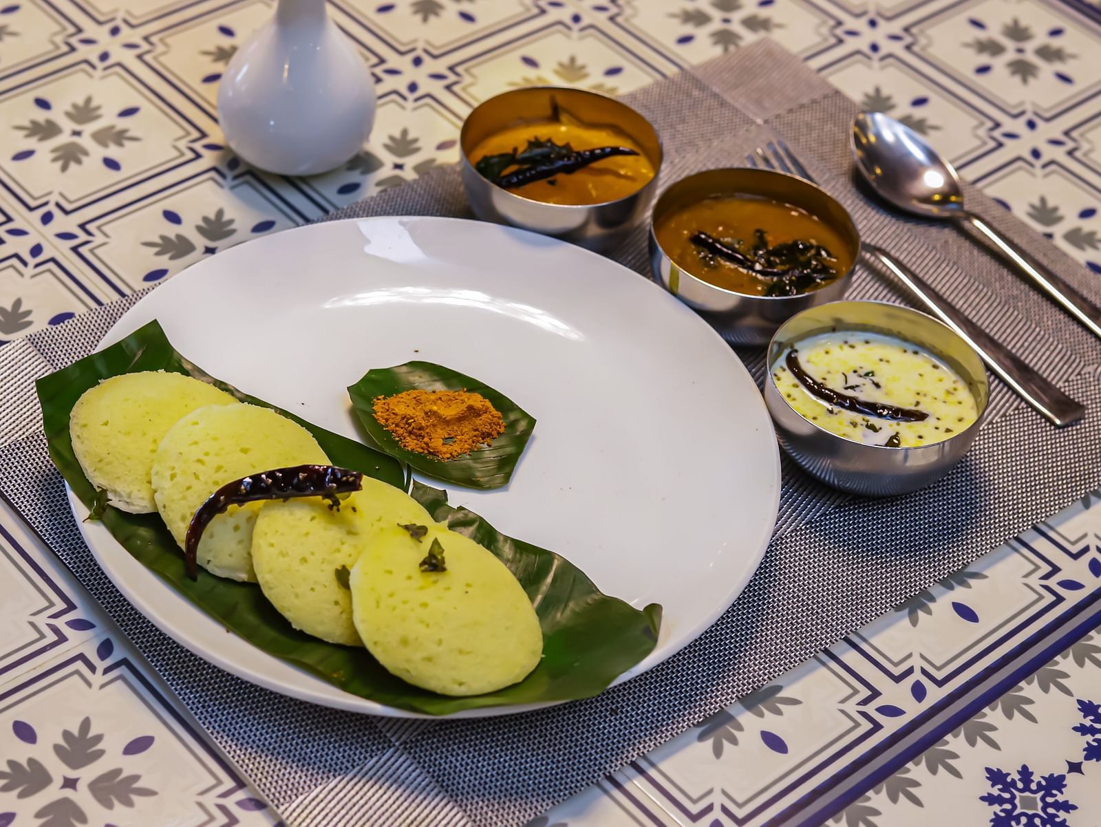 A white plate with food, accompanied by small bowls of sauces, rests on a patterned table at Vedikant Resorts The Mallard Corbett.