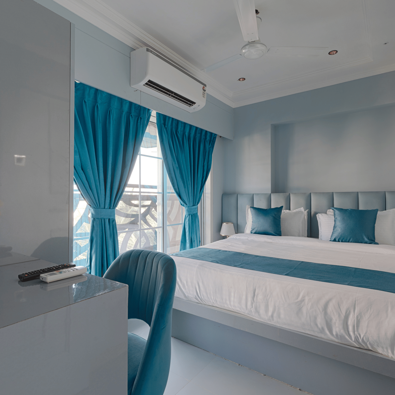 A bright bedroom featuring a queen bed with blue accents, a work desk, and vibrant blue curtains - Home2 Residency, Mumbai Airport
