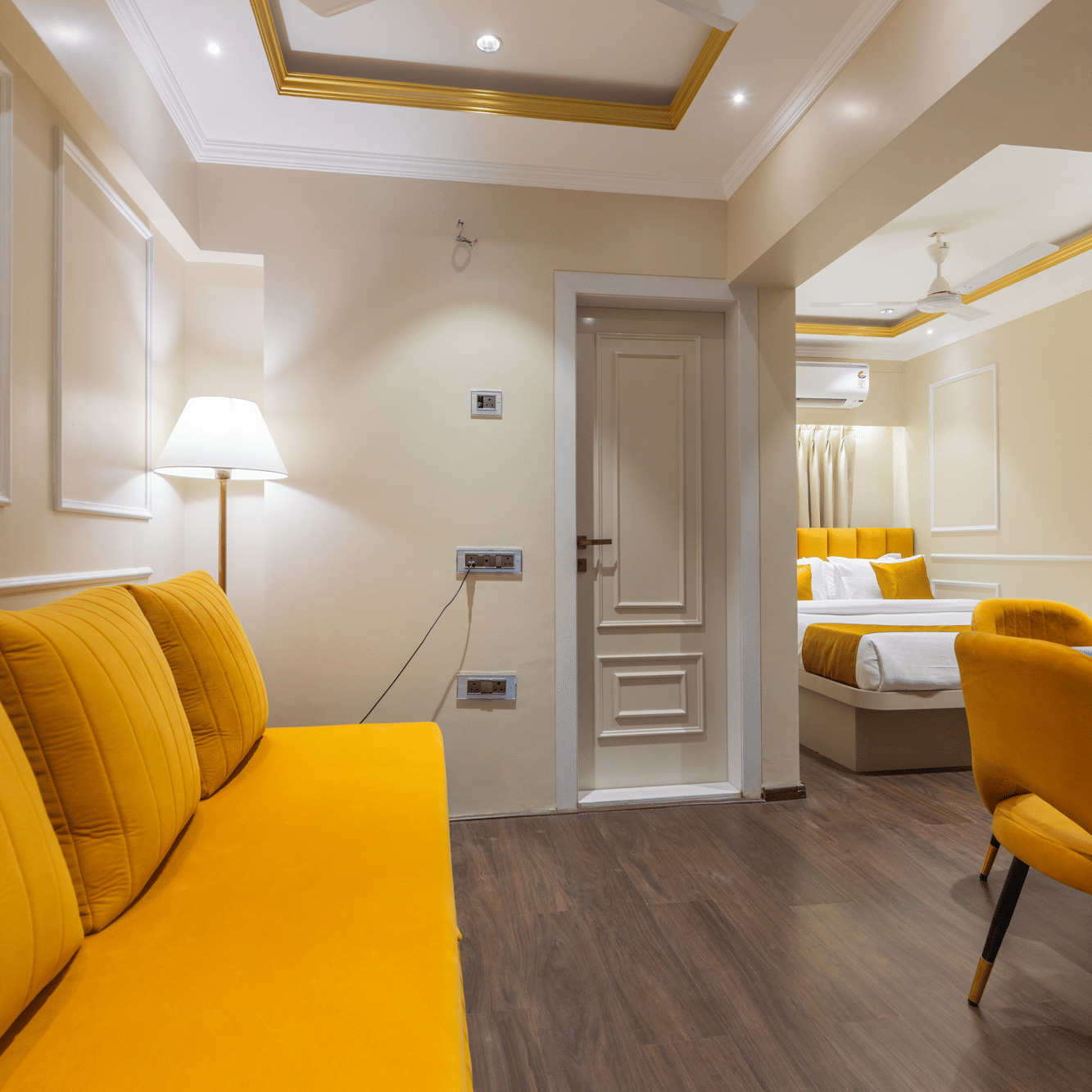 A cosy suite interior showing a yellow couch and a small dining area with a work desk and chair - Home2 Residency, Mumbai Airport