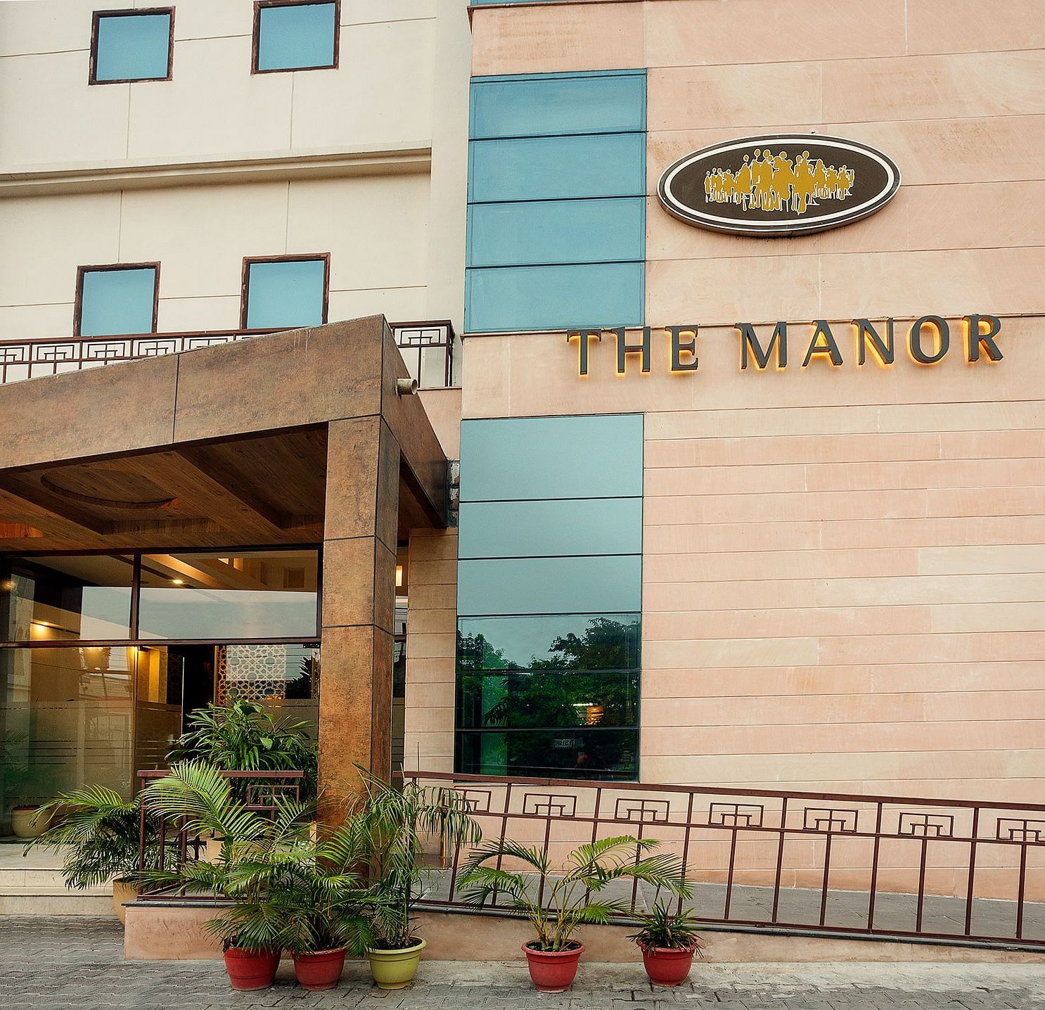 facade image of The Manor hotel, showcasing a modern entrance with potted plants and a clear blue sky above - The Manor, Bareilly