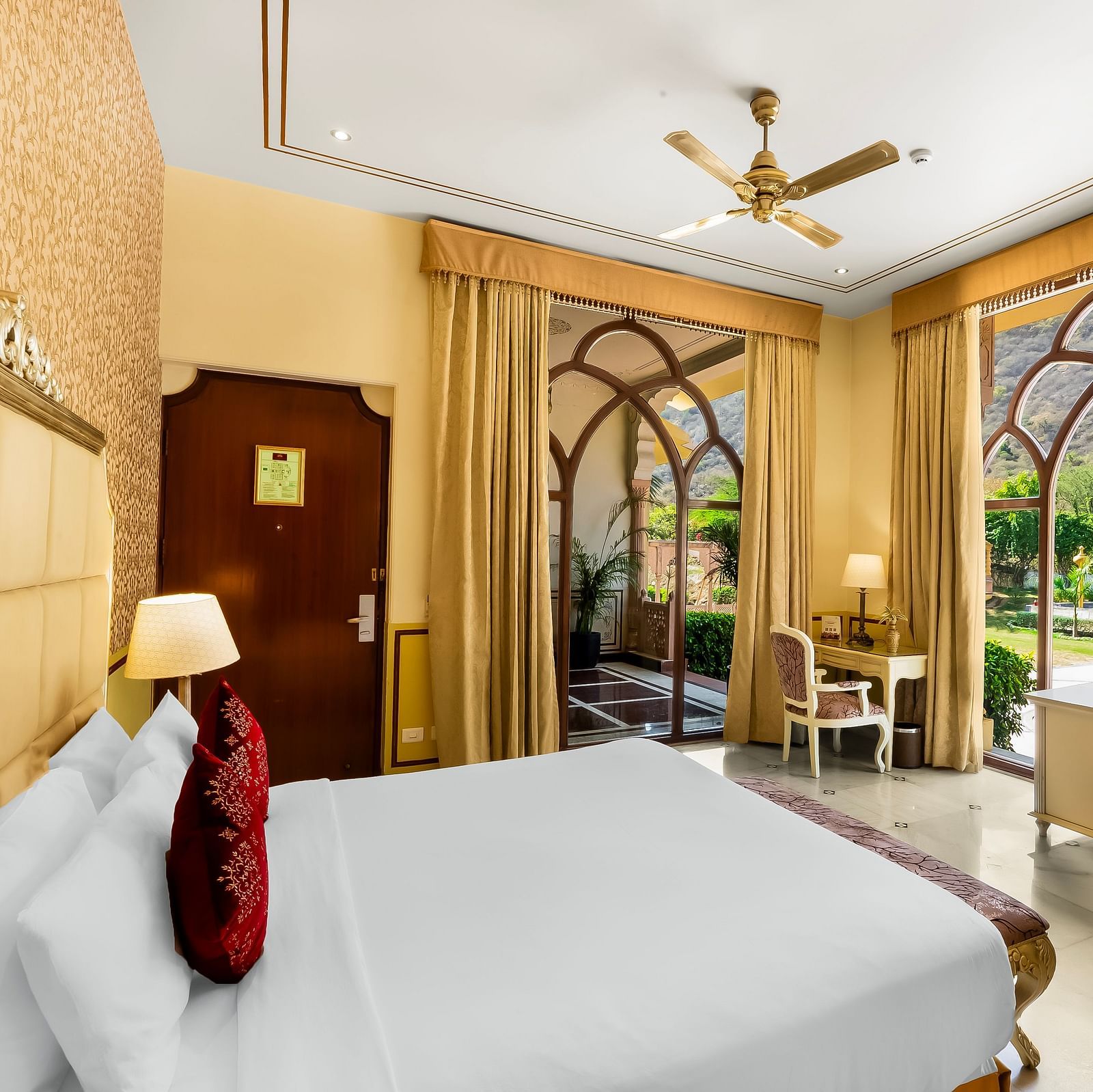 Luxurious suite at Rajasthali Resort Jaipur featuring canopy bed, royal seating area, and grand arched windows.