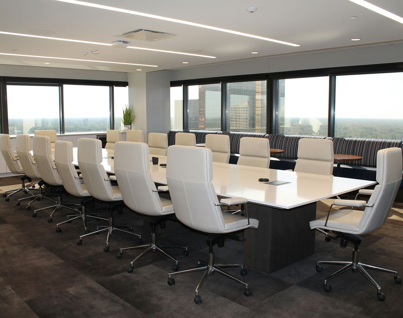 A modern conference room with a long table, white chairs, and large windows overlooking a city view.