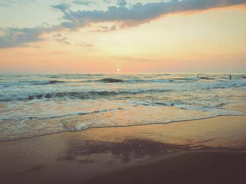 Seaside view of a sandy beach at sunset with gentle waves washing ashore.