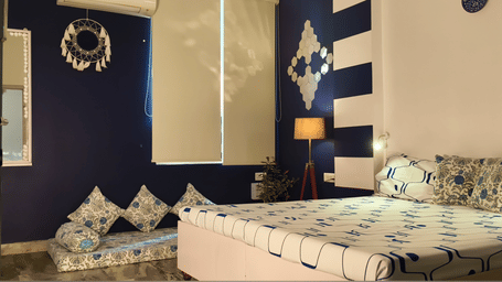 A Deluxe Room at Jaypore360 Homestay featuring a spacious bed, patterned wall decoration, a dream catcher, and an A/C unit.