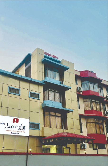 Exterior view of Pemaling Lords Eco Inn Guwahati featuring a multi-story building with architectural bay windows, a covered entrance canopy, a manicured lawn, and an edit icon overlay in the top right corner.