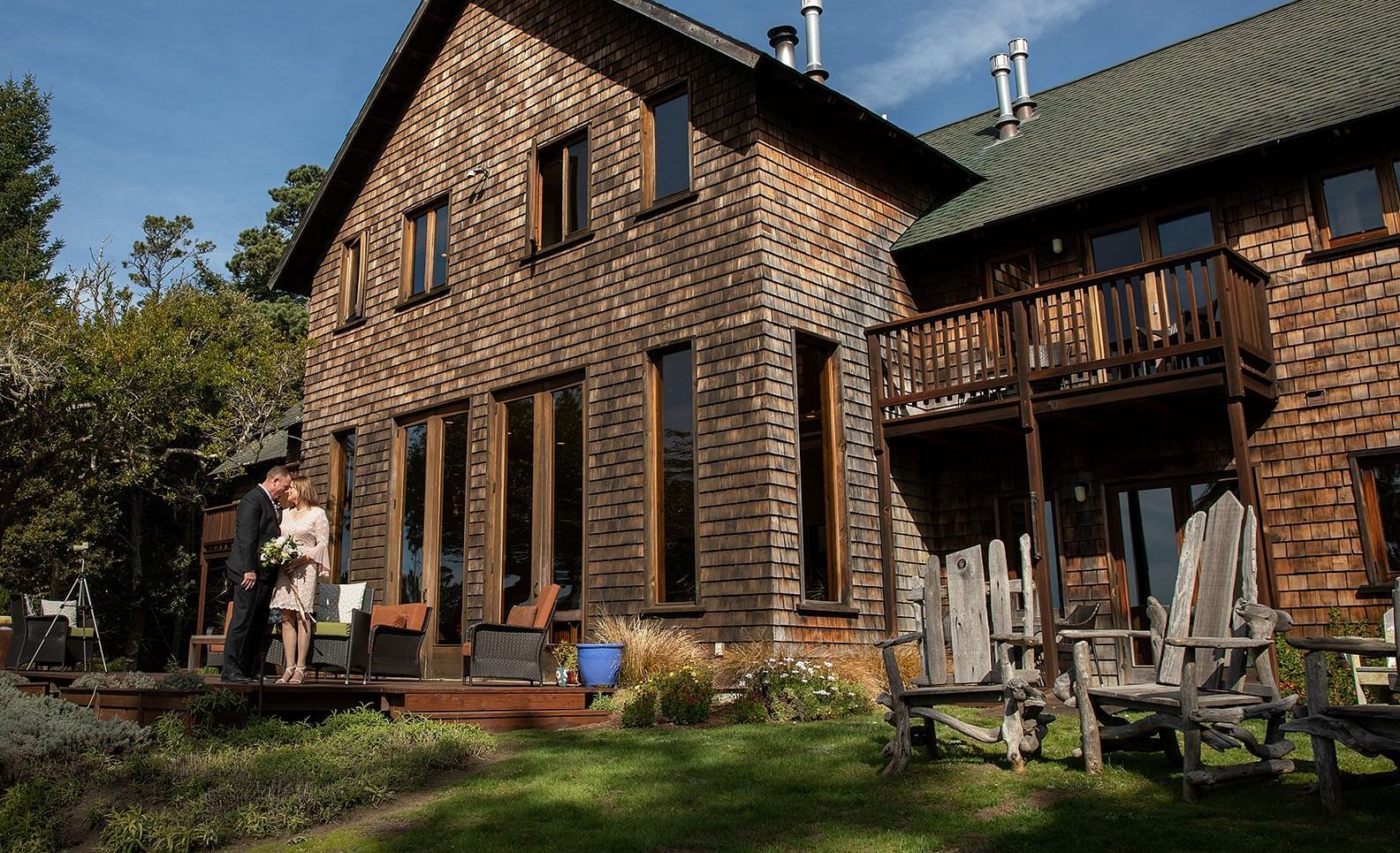 A couple posing in front of a charming rustic house surrounded by nature