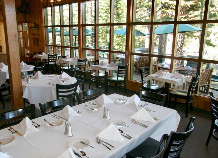 Kit Carson Lodge restaurant with set tables, wooden walls, and large windows overlooking trees.