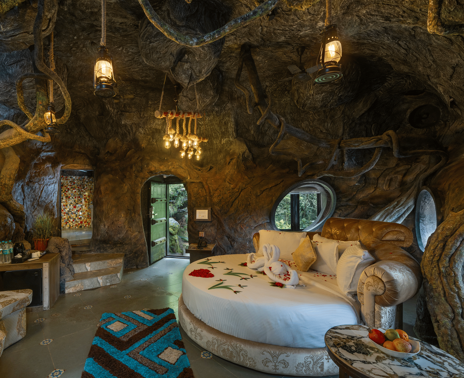 The bedroom of the Cave Room at Parakkat Nature Hotel and Resorts, Munnar, featuring a large circular bed, decorative light fixtures, and walls designed to resemble natural rock formations.
