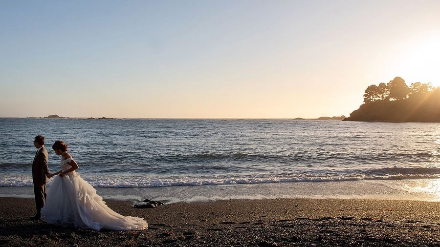 Bride and groom walking on the beach with golden sunlight reflecting on the waves