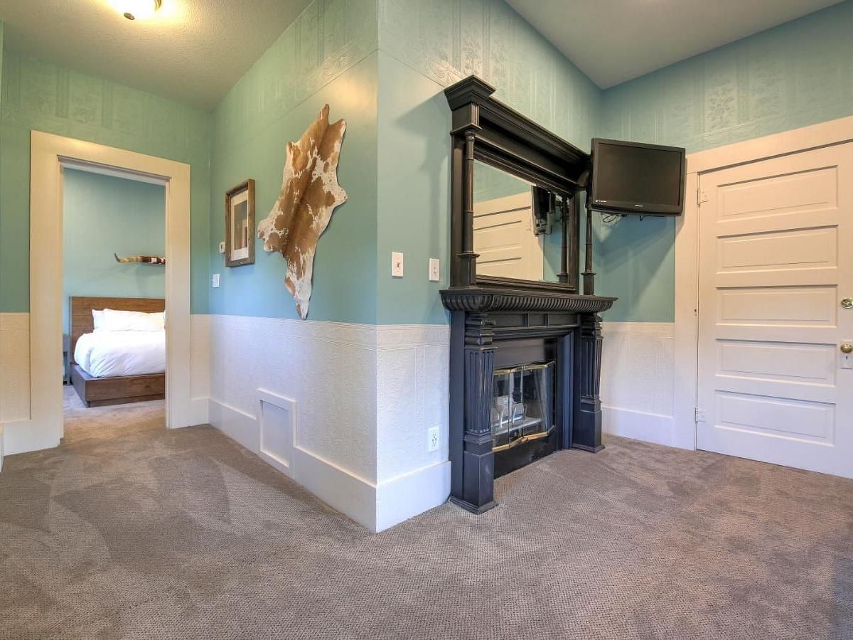 he Groveland Hotel's living area showcases sage green walls, an ornate black fireplace, mounted TV, and distinctive animal hide wall decor.
