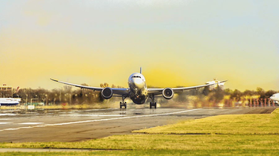 A wide-body passenger aircraft on a runway with landing gear down at sunset, with another aircraft visible on the right and grass verge in the foreground.