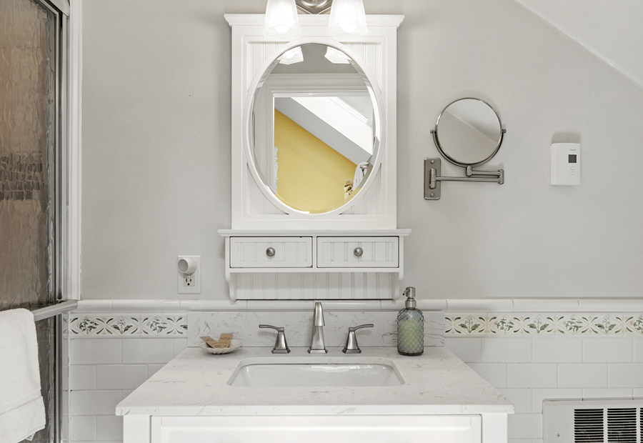 A clean and well-lit bathroom vanity with a white cabinet, marble countertop, and tile backsplash.