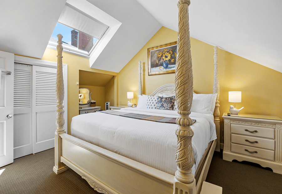 A wide view of a guest room with a four-poster bed, yellow walls, and a skylight.