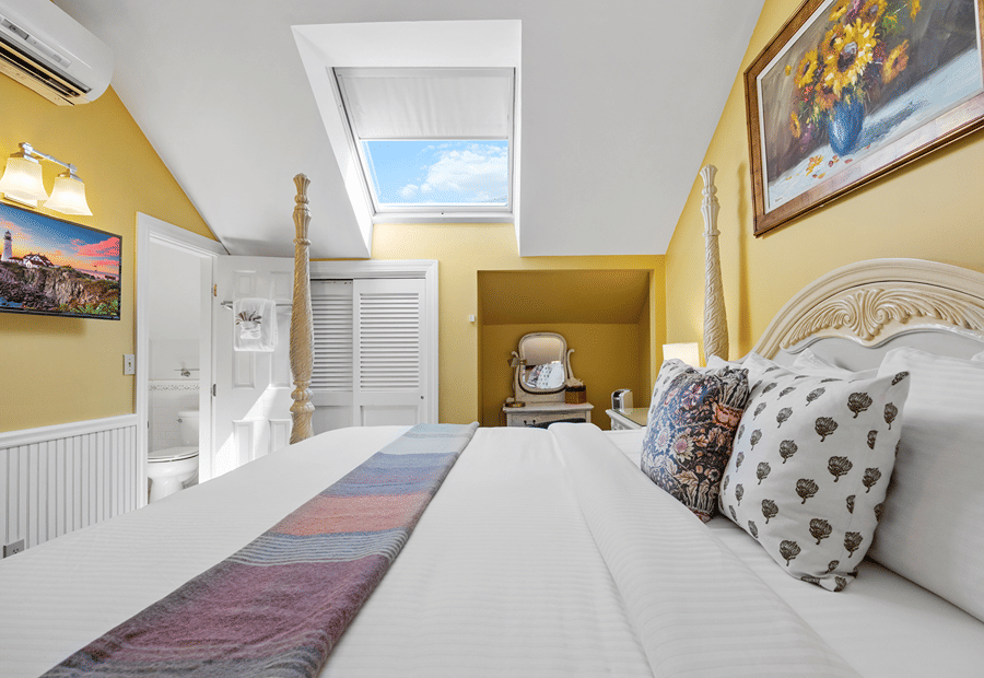 A bright and airy hotel room with a large bed, yellow walls, and a skylight.
