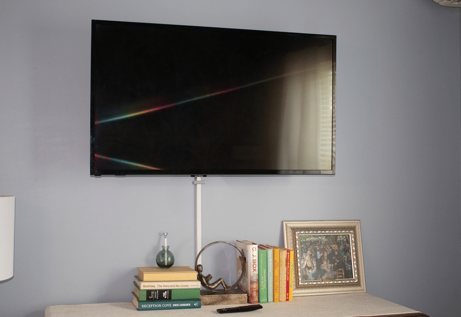 A wall-mounted TV above a dresser with books and decorative items