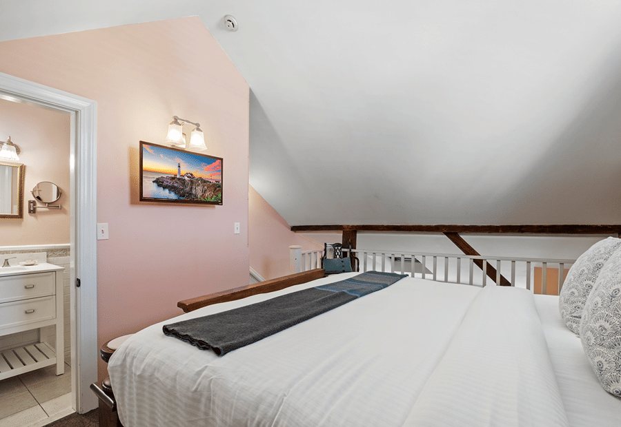 A cozy guest room with a large bed, pink walls, and a bathroom in suite.